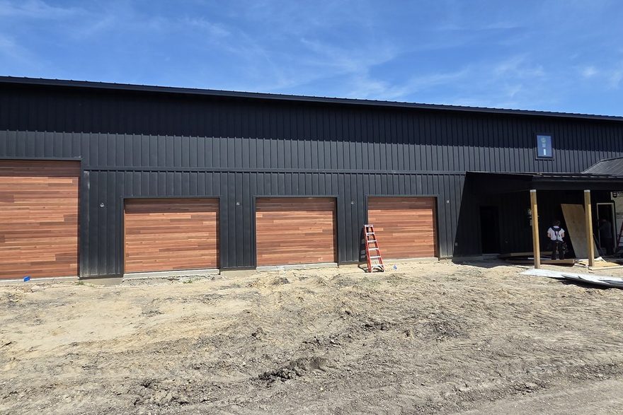 Oakmont black post-frame shop with wood-tone overhead doors, near completion
